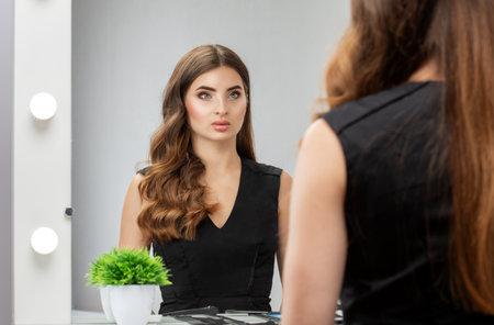 Hairdresser and make-up artist doing hair and makeup to a young attractive woman in a black dress in a beauty salon.の写真素材