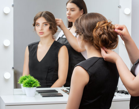 The hairdresser makes a hairstyle to a young attractive woman with a beautiful make-up in a black dress in a beauty salon.の写真素材