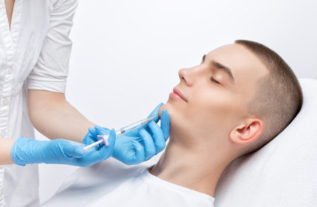 Men's cosmetology. Beautician makes a man a rejuvenation injection procedure of a handsome young man in a beauty salon. Professional make-up and face care.の写真素材