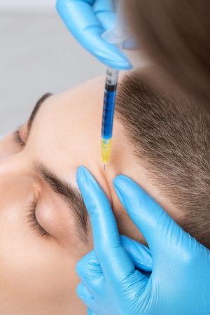 Men's cosmetology. Beautician makes a man a rejuvenation injection procedure of a handsome young man in a beauty salon. Professional make-up and face care.の写真素材