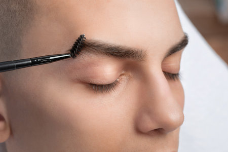 The makeup artist plucks the eyebrows of a handsome young man. Professional make-up and face care.の写真素材