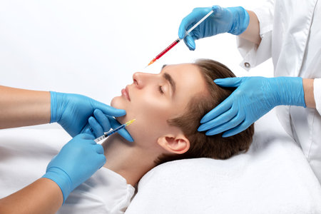 Men's cosmetology. Beautician makes a man a rejuvenation injection procedure of a handsome young man in a beauty salon.の写真素材