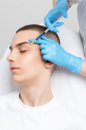 Men's cosmetology. Beautician makes a man a rejuvenation injection procedure of a handsome young man in a beauty salon.の写真素材