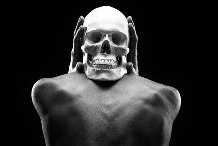 A thin woman sits with her back turned and holds a human skull in her hands.On a black background. one of the halloween symbolsの写真素材