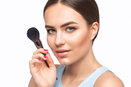 Portrait of a beautiful brunette girl with beautiful fresh makeup and healthy clean skin.Makeup artist holds a powder brush in her hands. professional makeup conceptの写真素材
