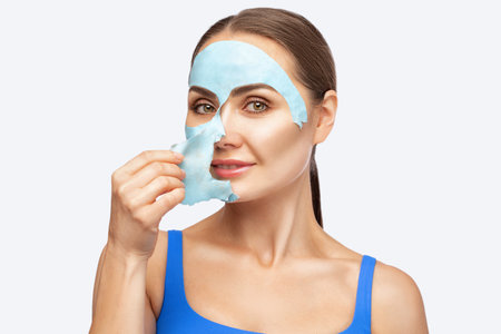 A beautician makes an alginate blue face mask for a woman's face to rejuvenate her skin. Cosmetological treatment of problem skin of the face and body.の写真素材