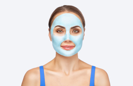 A beautician makes an alginate blue face mask for a woman's face to rejuvenate her skin. Cosmetological treatment of problem skin of the face and body.の写真素材