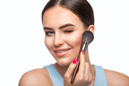 Portrait of a brunette girl with beautiful fresh makeup and healthy clean skin. She holds a powder brush in her hands. professional makeup conceptの写真素材