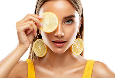 Portrait of an attractive girl with healthy clean skin and beautiful makeup she has earrings with a slice of lemon. Aesthetic cosmetology and make-up concept.の写真素材