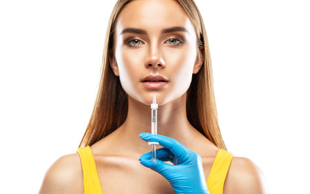 Cosmetologist does injections for lips augmentation anti wrinkle injections on the face of a beautiful woman in a yellow blouse. Female aesthetic cosmetology in a beauty salon.の素材 [FY310200639064]