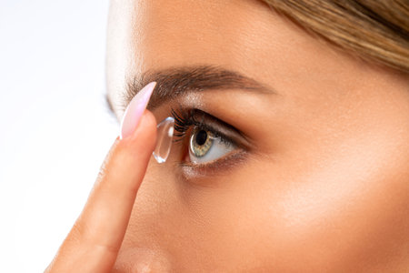 Beautiful blue eyed young woman holding a contact lens on her finger. Eye care and choice of means to improve vision.の写真素材