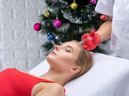 The cosmetologist makes anti-aging anti-wrinkle injections on the face of a beautiful woman. Women's aesthetic cosmetology in a beauty salon. New year concept.の写真素材