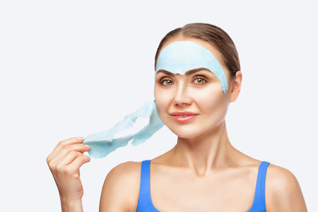 A beautician makes an alginate blue face mask for a woman's face to rejuvenate her skin. Cosmetological treatment of problem skin of the face and body.の写真素材