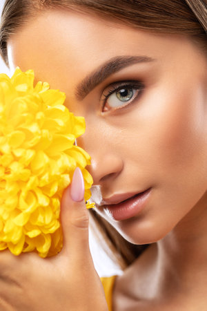 Portrait of an attractive girl with healthy clean skin and beautiful makeup, she is holding a yellow chrysanthemum. Aesthetic cosmetology and make-up concept.の写真素材