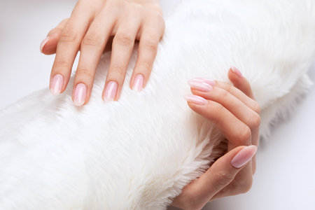 Girl's hands with a beautiful pale pink manicure. In the hands of white fur. the nail extension procedure in a beauty salon. professional hand care.の写真素材