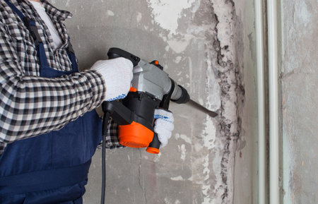 The builder with hammer drill perforator equipment making a hole in wall at construction site. Repair work, interior decoration of walls.の写真素材