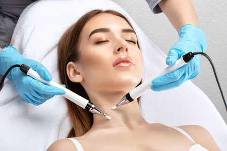 A doctor cosmetologist makes a microcurrent facial therapy to a young woman with a device in a beauty wellness salon.Cosmetology and professional skin care.の写真素材