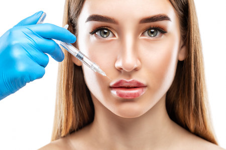 Cosmetologist does injections for lips augmentation anti wrinkle injections on the face of a beautiful woman. Female aesthetic cosmetology in a beauty salon.の写真素材