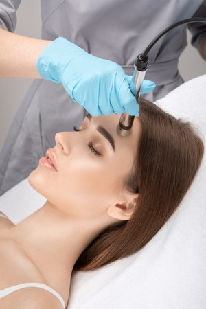 A doctor cosmetologist makes a microcurrent facial therapy to a young woman with a device in a beauty wellness salon.Cosmetology and professional skin care.の写真素材