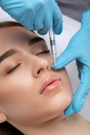 Cosmetologist does injections for lips augmentation and anti wrinkle in the nasolabial folds of a beautiful woman. Women's cosmetology in the beauty salon.の写真素材