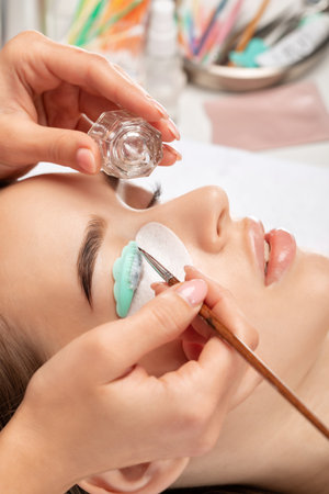 Make-up artist makes the procedure of lamination and dyeing of eyelashes to a beautiful woman in a beauty salon. Eyelash extensions. Eyelashesの写真素材