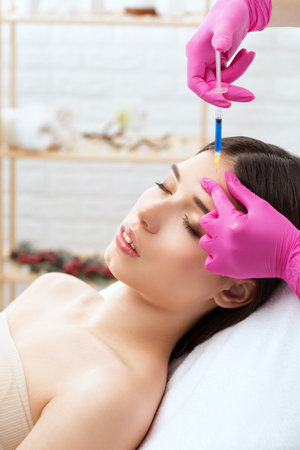 Cosmetologist makes rejuvenating anti wrinkle injections on the face of a beautiful woman. Female aesthetic cosmetology in a beauty salon.の写真素材