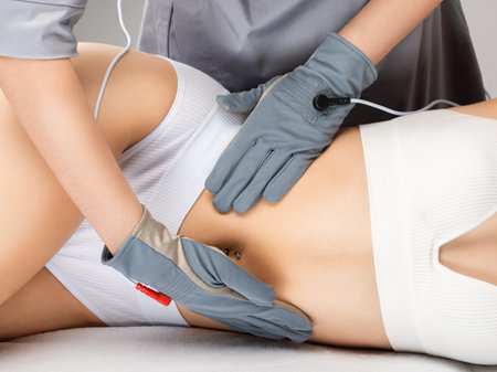 Doctor cosmetologist makes a microcurrent massage procedure on the belly of a beautiful girl in a beauty salon.の写真素材