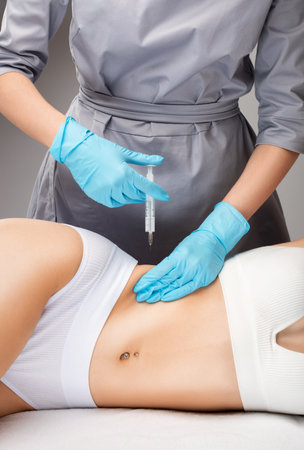 cosmetologist makes lipolytic injections to burn fat on the stomach and waist of a woman. Female aesthetic cosmetology in a beauty salon.Cosmetology concept.の写真素材
