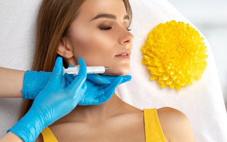 Beautician makes anti-aging injections against fat deposits on the chin of a beautiful woman. Women's aesthetic cosmetology in a beauty salon.の写真素材