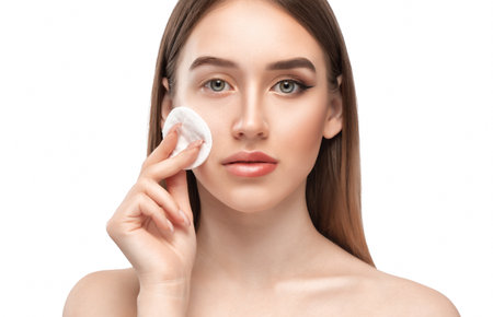 A young beautiful girl removes makeup with a cotton pad and micellar water from her face and eyes.の写真素材