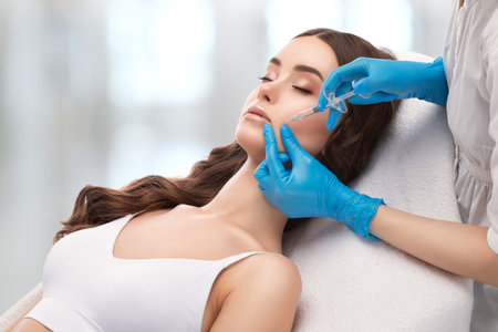 Cosmetologist does injections for lips augmentation and anti wrinkle in the nasolabial folds of a beautiful woman. Women's cosmetology in the beauty salon.の写真素材