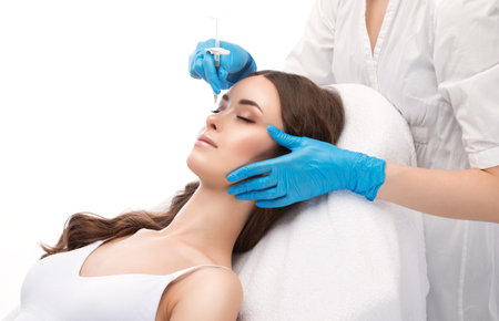 The cosmetologist makes injections to correct the curvature of the nose of a beautiful woman. Women's aesthetic cosmetology in a beauty salon.の写真素材
