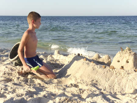 Boy playing on the beach and building sand castleの写真素材