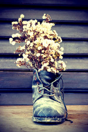 Old ruined boot is used as a vase for wild flowers - vintage stylized photoの写真素材