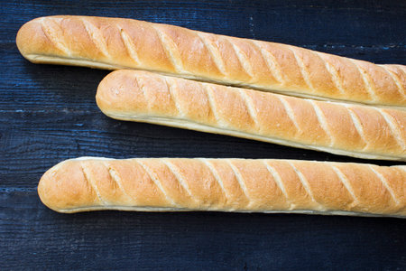 Fresh baguette on a dark wooden  background, horizontal view from above