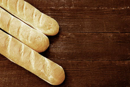 Three fresh baguettes on the wooden background. Vintage filter effect used.の写真素材