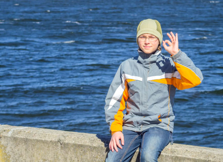 A boy sits on the banks of the Dnieper River and showing thumbs OK
