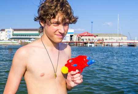 Boy playing with water pistol on a background of a seaの写真素材