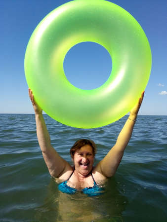 A woman holds the inflatable buoy standing in a sea laughingの写真素材