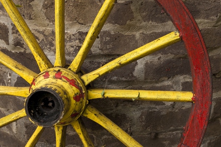 detail of old wagon wheel with metal rim leaning on a stone wallの写真素材