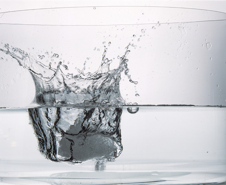 large ice cube splashing into a glass of waterの写真素材