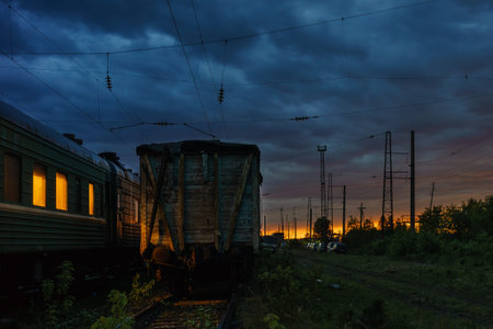 Colorful sunset with sky at the railway station in summer. The windows of the passenger car are lit.