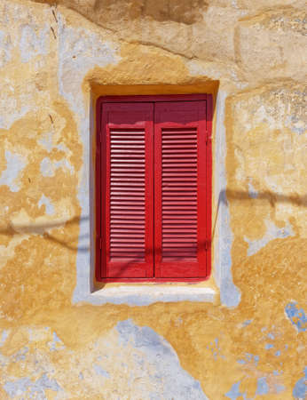 deep red window shutters on weathered colorful wall, Athens Greece, Anafiotika neighborhoodの写真素材