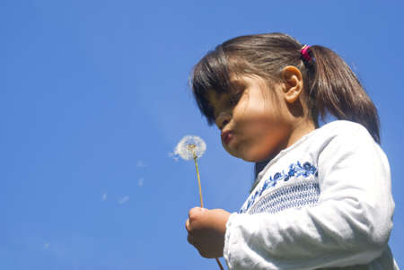 Girl blowing dandelion against blue skyの写真素材
