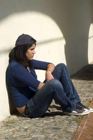 Sad girl sitting against a wallの写真素材