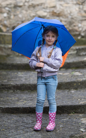 Little girl playing in the rain under umbrellaの写真素材