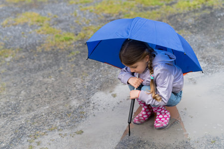 Little girl playing in the rain under umbrellaの写真素材