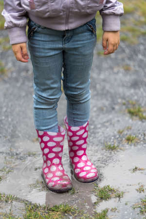 Legs of child in rubber boots jumping in autumn puddleの写真素材