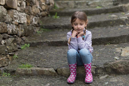 Little girl sitting on the stairs on rainy dayの写真素材