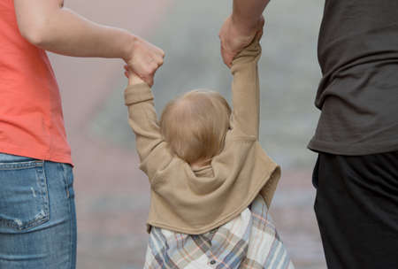 Back view of little girl holding hands of parentsの写真素材